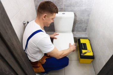 Profesyonel tesisatçı tuvaletteki klozeti tamir ediyor.