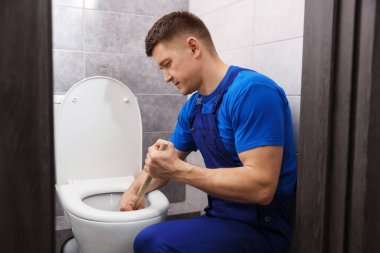Tesisatçı içeride pompayla tuvaletin tıkanmasını açıyor.