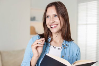 Evde gözlüklü ve kitaplı gülümseyen genç kız.