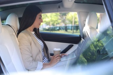 Modern arabasında kahve ve dizüstü bilgisayarı olan bir kadın, dışarıdan manzaralı.