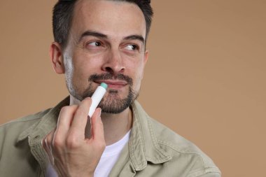 Yakışıklı bir adam açık kahverengi arka planda dudaklarına merhem sürüyor.