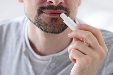 Bulanık ışık arka planında dudaklarına dudak kremi süren bir adam.