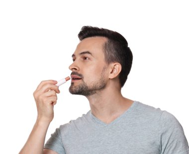 Beyaz arka planda dudaklarına dudak kremi süren yakışıklı bir adam.