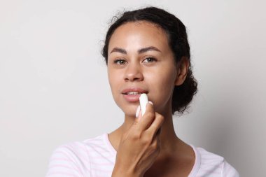 Gri arka planda dudaklarına merhem süren güzel bir kadın.