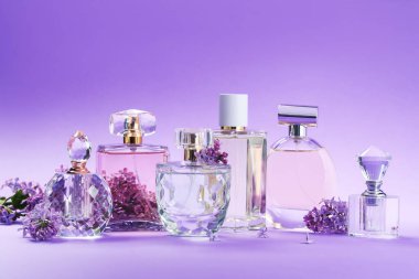 Parfümlü şişeler ve mor arkaplanda leylak çiçekleri, yakın plan.
