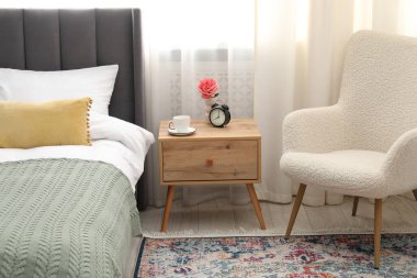 Yatağın yanında kahve, çiçek ve çalar saat olan komodinin yanında.