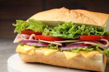 Gri masadaki jambonlu, peynirli ve sebzeli baget sandviç, bulanık kahverengi arka plan, yakın plan.