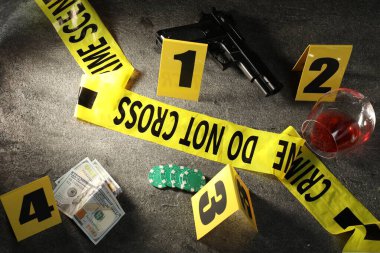 Adli tıp uzmanı. Sarı suç mahalli bandı, işaretler ve kanıtlar gri masada, üst tarafta.