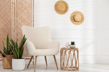 Rahat koltuk, yan masa ve beyaz duvarın yanındaki bitkiler.