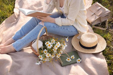 Bir buket kır çiçeğiyle çayırda kitap okuyan bir kadın, yakın plan.