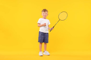 Badminton raketi olan küçük bir çocuk ve sarı arka planda küçük bir horoz.