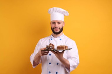 Üniformalı mutlu pastacı turuncu arka planda çikolatalı tatlılar tutuyor.