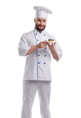 Üniformalı mutlu pastacı beyaz arka planda yaban mersinli lezzetli tart tutuyor.
