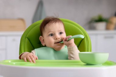 Evdeki beslenme sandalyesinde yemek yiyen şirin bir bebek.