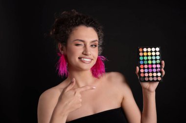 Gülümseyen kadın, siyah arka plandaki parlak göz falı paletine işaret ediyor.