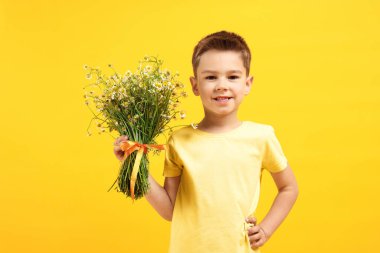 Sarı arka planda bir buket güzel papatya çiçeğiyle gülümseyen küçük çocuk