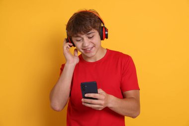 Sarı arka planda akıllı telefonlu, kulaklıklı, gülümseyen genç çocuk.