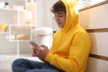 Ergen çocuk evde çekmecelerin yanında akıllı telefon kullanıyor.