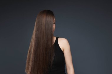 Sağlıklı, uzun saçlı, koyu gri arka planda genç bir kız. Metin için boşluk