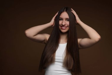 Kahverengi arka planda sağlıklı uzun saçlı gülümseyen genç kızın portresi.