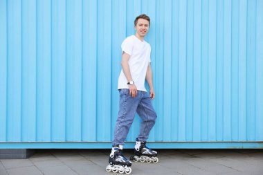 Açık mavi duvarın yanında patenli mutlu genç adam