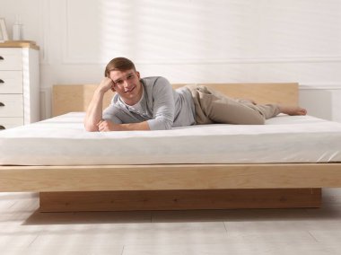 Genç adam evde yumuşak bir döşekle yatakta yatıyor.