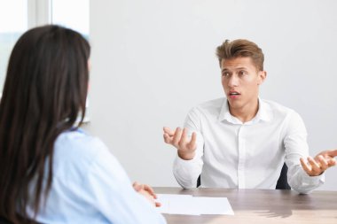 Ahşap masada oturan genç bir adam kadınlara şikayette bulunuyor.