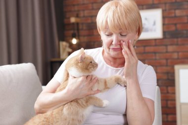 Yaşlı kadın evdeki kanepede kedisiyle alerji geçiriyor.