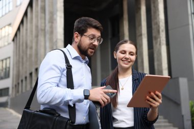 Ofis binasının yakınında tabletli ve akıllı telefonlu mutlu iş arkadaşları