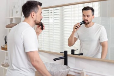 Yakışıklı adam evde aynanın yanında tıraş makinesiyle tıraş oluyor.