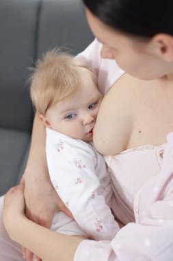 Anne küçük bebeğini kanepede emziriyor.