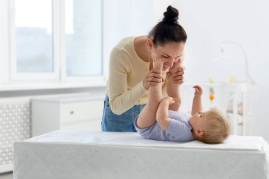 Anne, sevimli bebeğiyle evde masasını değiştirirken oynuyor.