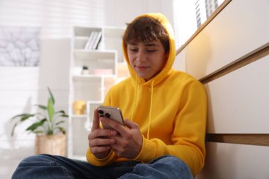 Ergen çocuk evde çekmecelerin yanında akıllı telefon kullanıyor.