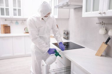 Koruyucu kıyafetli haşereci evde böcek ilacı sıkıyor.