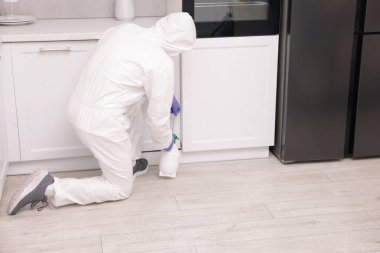 Koruyucu kıyafetli haşereci evde böcek ilacı sıkıyor.