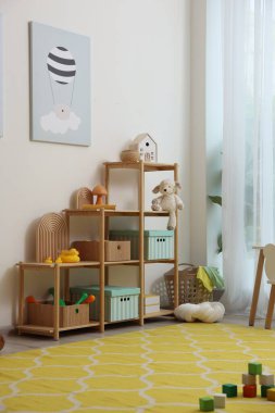 Süslü oyun odasındaki beyaz duvarın yanında dekorlu ve oyuncaklı raf ünitesi. İç tasarım