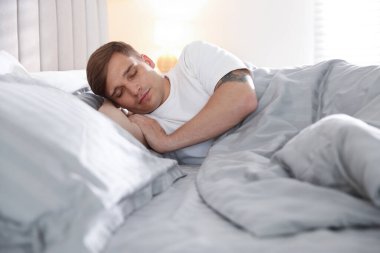 Evdeki yumuşak yatakla yatakta uyuyan genç adam.