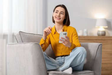 Evdeki koltukta modern akıllı telefon kullanan bir kadın.