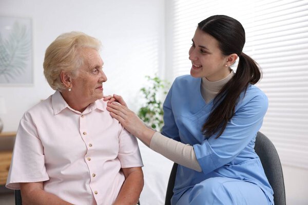 Nurse assisting senior woman indoors. Home health care service