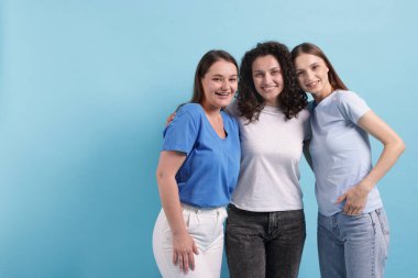 Açık mavi arkaplanda kucaklaşan üç arkadaş, metin için boşluk