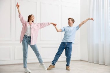 Mutlu çift evde beyaz duvarın yanında dans ediyor.
