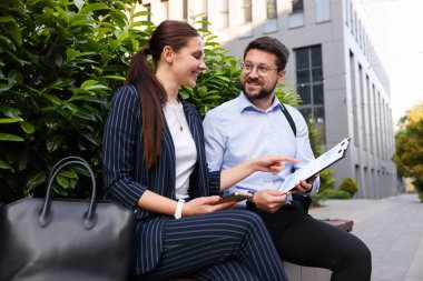 Mutlu iş arkadaşları ofis binasının yanındaki bankta bir şeyler tartışıyor.