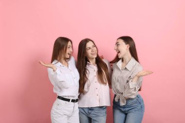 Arkadaşlar pembe arka planda birbirlerine sarılıyorlar.