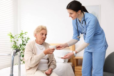 Hemşire içerideki yaşlı kadına bir bardak su veriyor. Ev sağlık hizmetleri