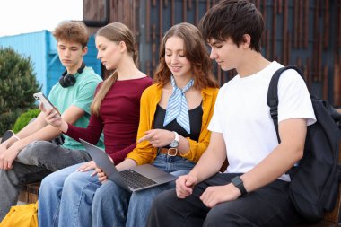 Parktaki bankta farklı cihazları olan gençler