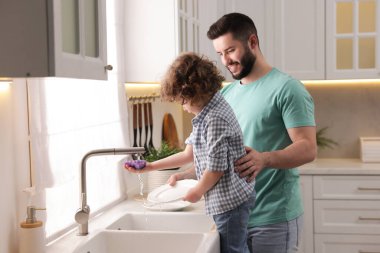 Baba ve oğlu evde birlikte bulaşık yıkıyorlar.