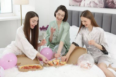 Pijama partisi. Gözlüklü mutlu arkadaşlar evde pizza yiyorlar.