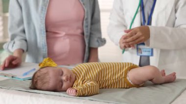 Anne ve sevimli küçük çocuğunun hastanede çocuk doktoruyla randevusu var. Doktor steteskopla uyuyan bebeği muayene ediyor.