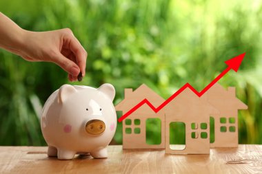 Gayrimenkul değerini arttır. Kadın açık hava kumbarasına para koyuyor, yakın plan. Ev modelleri ve ok