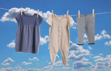Mavi gökyüzüne karşı çamaşır ipinde kurumuş farklı bebek kıyafetleri.